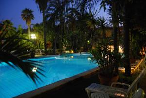a swimming pool with palm trees at night at Garden Hotel Catania in San Giovanni la Punta