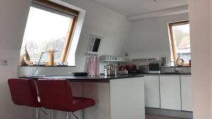 レムシャイトにあるStadtvilla Kö97 - Apartment Relaxのキッチン(白いキャビネット、赤い椅子付きのカウンター付)