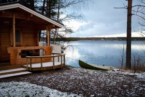 a cabin with a boat on the shore of a lake at Hiekkarannanlomat in Kannonkoski