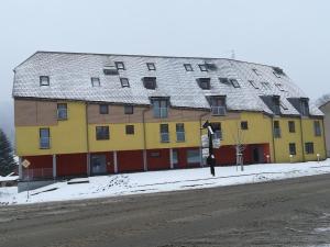 un grand bâtiment jaune et rouge dans une rue enneigée dans l'établissement Apartmán Deštná čp.1, à Deštné v Orlických horách