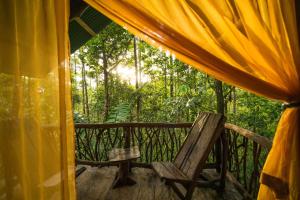 uma cadeira de madeira num alpendre com uma tenda em La Tigra Rainforest Lodge em La Fortuna