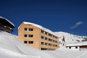 un edificio cubierto de nieve frente a una montaña en WarthsAp Apartmenthaus, en Warth am Arlberg