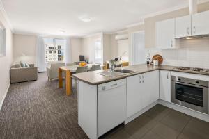 a kitchen with white cabinets and a living room at Quest Wollongong in Wollongong