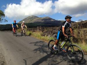 drie mensen fietsend over een weg met bergen op de achtergrond bij Black Lava Hostel and Lodge in Kintamani