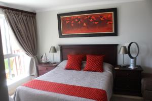 ein Schlafzimmer mit einem Bett mit roten Kissen und einem Gemälde in der Unterkunft Seafront Apartment in Mossel Bay in Mossel Bay