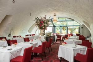 un comedor con mesas blancas y sillas rojas en Bilderberg Château Holtmühle, en Venlo