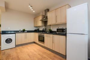 a kitchen with wooden cabinets and a white refrigerator at Portland Square - 2 Bedroom Modern City Apartment in Nottingham