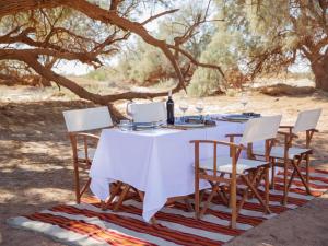 a table with chairs and wine glasses on it at Nubia Luxury Camp Erg Chegaga in El Gouera