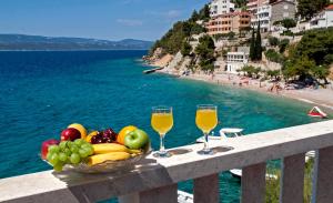 eine Schale Obst und 2 Gläser Wein auf einem Balkon mit Blick auf den Strand in der Unterkunft Apartments Ljiljana in Mimice