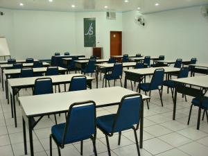 an empty classroom with tables and blue chairs at Js Palace Hotel in Alfenas