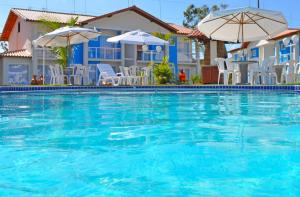 uma grande piscina azul com cadeiras brancas e guarda-sóis em Ap (Flat) Taperapuã Porto Seguro em Porto Seguro