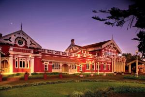 a large red house with a yard at WelcomHeritage Fernhills Royal Palace in Ooty