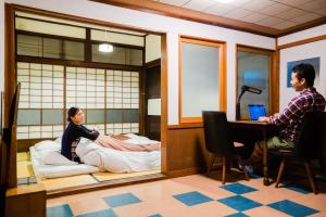 a man sitting at a desk in a room with a woman on a bed at Guest House Kura in Suzaka