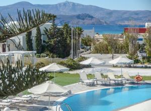 a pool with chairs and umbrellas next to the ocean at Birikos Studios & Apartments in Agios Prokopios