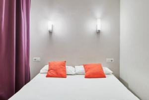 Una cama con dos almohadas naranjas encima. en Mayerling Schumann Barcelona, en Barcelona