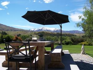 a wooden table with an umbrella and a bench at Waiorau Homestead in Cardrona