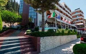un bâtiment avec des drapeaux et des escaliers en face de celui-ci dans l'établissement Hotel New York, à Vlorë