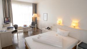 Habitación de hotel con cama blanca grande y escritorio. en Euro Park Hotel Hennef en Hennef