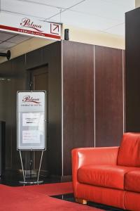 a red couch in front of a wall with a sign at Hotel Palma in Mažeikiai