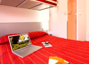 un ordenador portátil sentado en la parte superior de una cama roja en Premiere Classe Niort Est La Creche, en La Creche