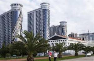two people walking in a park in front of tall buildings at ApartHotel Calypso in Orbi in Batumi