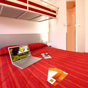 un ordenador portátil sentado en la parte superior de una cama roja en Hôtel Premiere Classe Pamiers, en Pamiers
