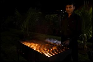 un homme debout devant un grill la nuit dans l'établissement Kunjwan Resort, à Bhor