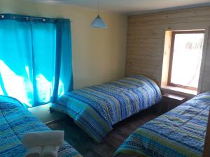 two beds in a room with blue curtains and a window at Cabañas Rincon del Sur in Cochrane
