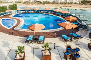 a beach with a pool, chairs, tables, and umbrellas at Ibis Abu Dhabi Gate in Abu Dhabi