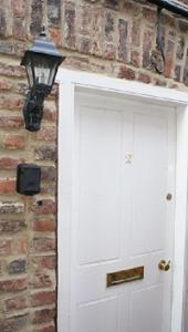 a white door with a light next to a brick wall at Laverick Steps in Whitby