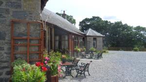 a stone building with chairs and a table with flowers at Meadowside Cottages in Balavil