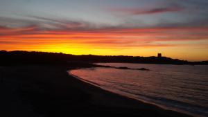 - un coucher de soleil sur la plage avec un phare au loin dans l'établissement On The Beach La Rena Beddha, à Aglientu