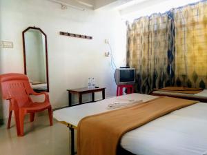 a bedroom with a bed and a chair and a tv at Hotel Ashwini Lodge in Mysore