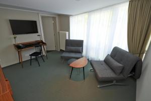 慕尼黑的住宿－Parkhotel Obermenzing，客厅配有两把椅子、一台电视和一张桌子
