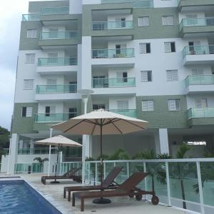 a pool with two chairs and an umbrella next to a building at Apartamento na Praia Grande - Ubatuba in Ubatuba