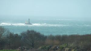 a lighthouse on a rock in the ocean with waves at Le Pilleur d'Epaves in Cléden-Cap-Sizun