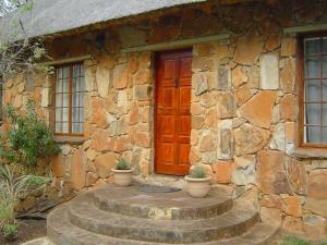 a stone house with a wooden door and some potted plants at Forest Creek Lodge & Spa in Badfontein