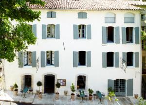 a white house with green shutters and tables and chairs at Hotel Restaurant des Deux Rocs in Seillans