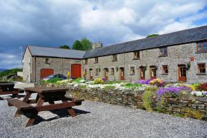 a stone building with two picnic tables in front of it at Cilhendre Holiday Cottages - The Dairy in Swansea