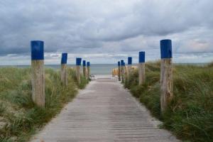 Burgtiefe auf Fehmarn 的住宿－Ferienwohnung-am-Suedstrand，通往海滩的木道,海滩上设有蓝色的柱子
