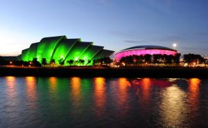 a building with green and pink lighting in front of the water at Clydebank Apartment in Glasgow