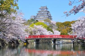 un puente rojo sobre un río con un castillo en el fondo en Himeji Park Hotel (Adult Only) en Himeji