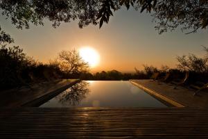 a pool with chairs and the sunset in the background at LAS JARILLAS Hostería & Bodega in San Javier
