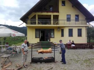 two men cooking chickens on a grill in front of a house at Grandemi Belvedere Bucovina in Frasin