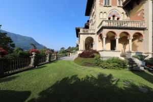 ein großes Haus mit einem Rasenplatz und einem Zaun in der Unterkunft Villa Castiglioni Luxury Apartment in Laglio