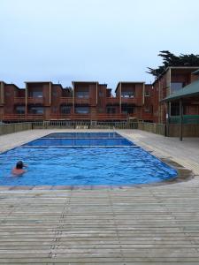 un uomo che nuota in una grande piscina con edifici sullo sfondo di Casa Frente al Mar a Pichilemu