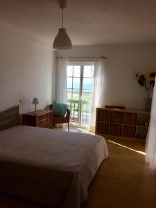 a bedroom with a bed and a window and a chair at Casa do Mar em Porto Covo in Porto Covo