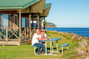a man and woman sitting at a table near the water at BIG4 Batemans Bay at Easts Riverside Holiday Park in Batemans Bay