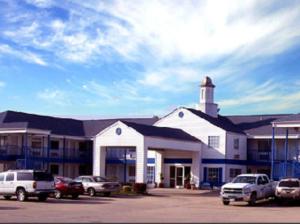 Un gran edificio blanco con coches aparcados en un estacionamiento. en American Inn and Suites White Hall, en White Hall