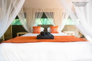 a bedroom with a bed with white curtains and orange pillows at Southern Sands Eco Lodge in Hoedspruit